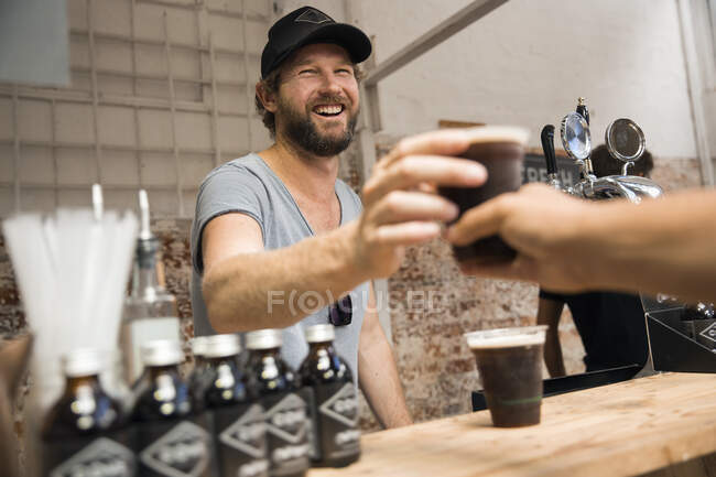 Titular de puesto masculino sirviendo café de cerveza fría en puesto cooperativo del mercado de alimentos - foto de stock