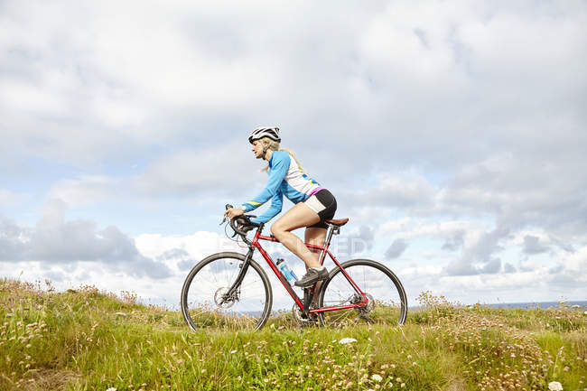 Cyclist riding past meadow on sunny day — Stock Photo