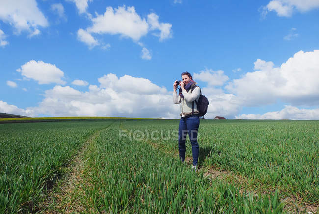Young woman standing in field, taking photograph of landscape — Stock Photo