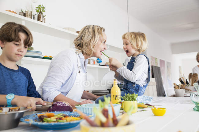 Chica alimentación madre espárragos en la mesa de la cocina - foto de stock