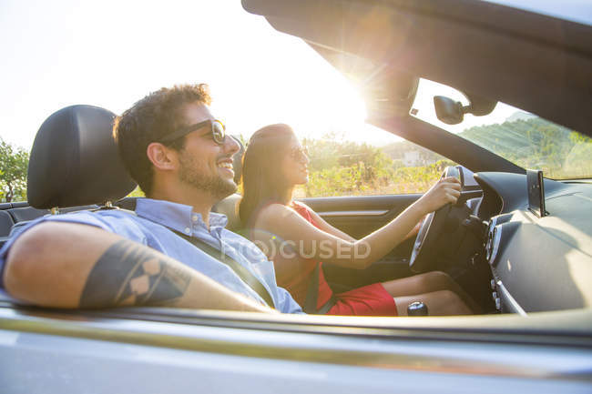 Casal jovem dirigindo na estrada rural iluminada pelo sol no conversível, Maiorca, Espanha — Fotografia de Stock