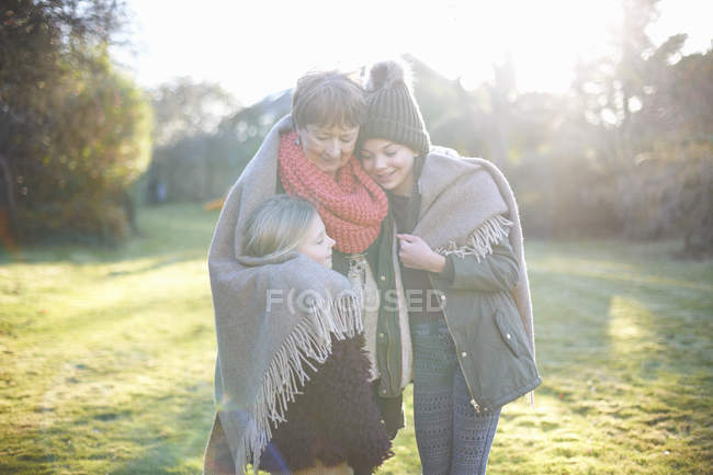 Бабуся і онуки обіймаються в саду разом під час холодної погоди — стокове фото