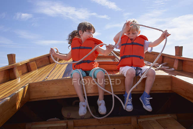 Two children sitting in boat in life jackets and holding rope — Stock Photo