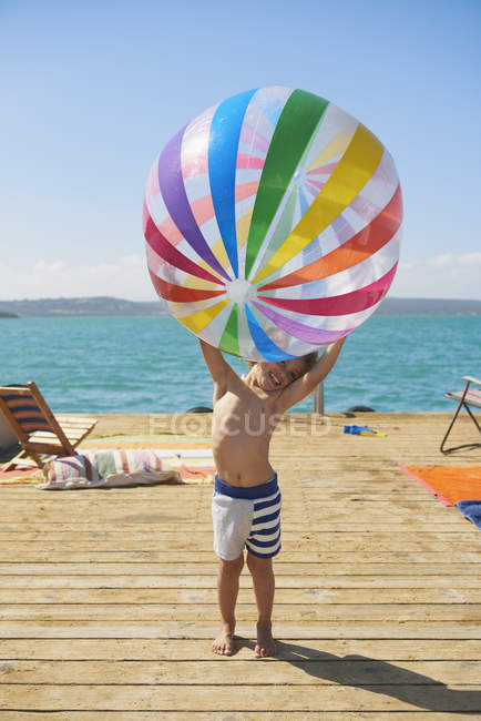 Niño sosteniendo pelota de playa en la cubierta del sol casa flotante, Kraalbaai, Sudáfrica - foto de stock