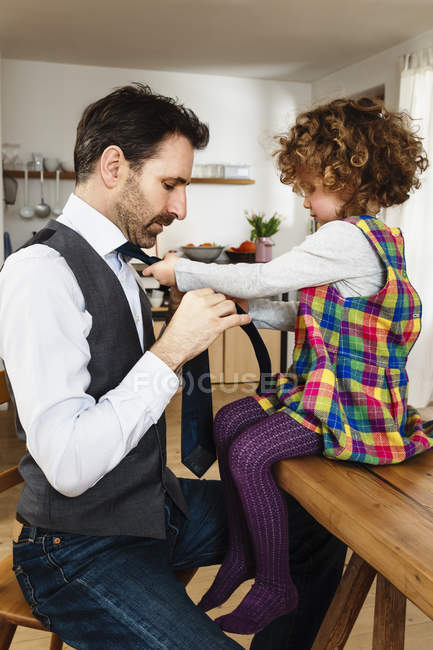 Vista lateral da menina amarrando gravata pai na cozinha — Fotografia de Stock