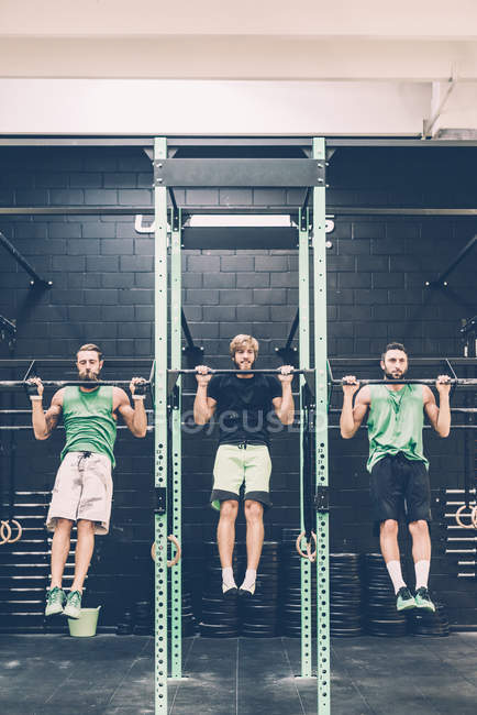 Two male cross trainers doing chin ups on exercise bar in gym — Stock Photo