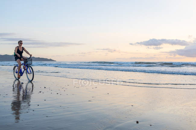 Frau radelt am Strand bei Sonnenuntergang, nosara, guanacaste provinz, costa rica — Stockfoto