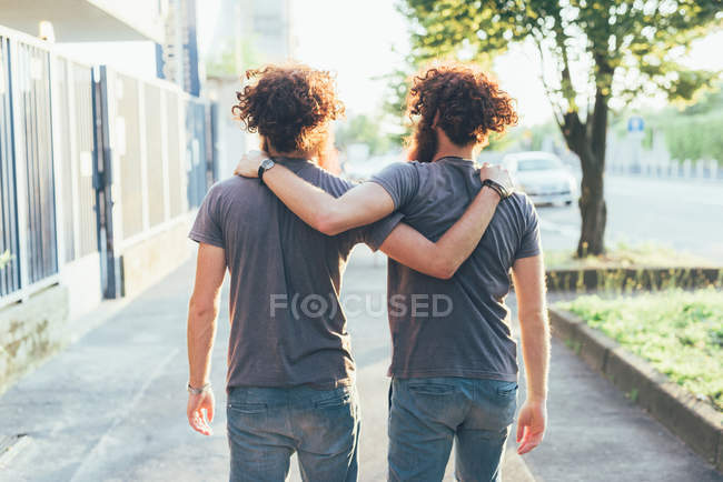 Rückansicht eineiiger männlicher erwachsener Zwillinge, die auf dem Gehweg spazieren gehen — Stockfoto
