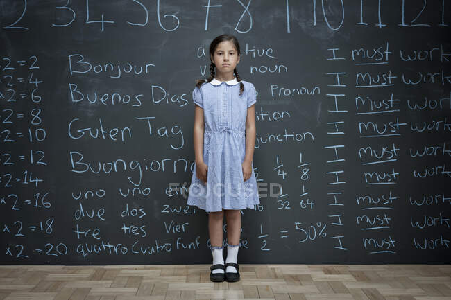 Retrato de la colegiala de pie frente a una gran pizarra con las tareas escolares con tiza en ella - foto de stock