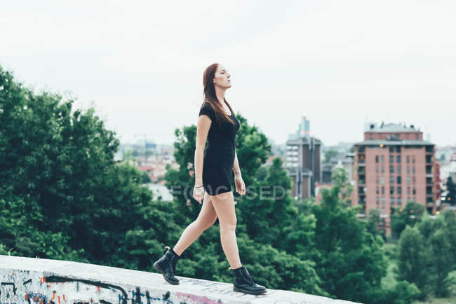 Young woman in mini dress walking on wall above city — Stock Photo