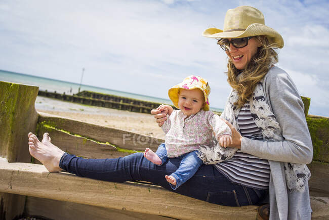 Mitte erwachsene Frau und kleine Tochter sitzen am Strand von Groyne, Ferring Beach, West Sussex, Großbritannien — Stockfoto