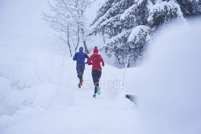 Rear view of male and female runners running on track in deep snow — Stock Photo
