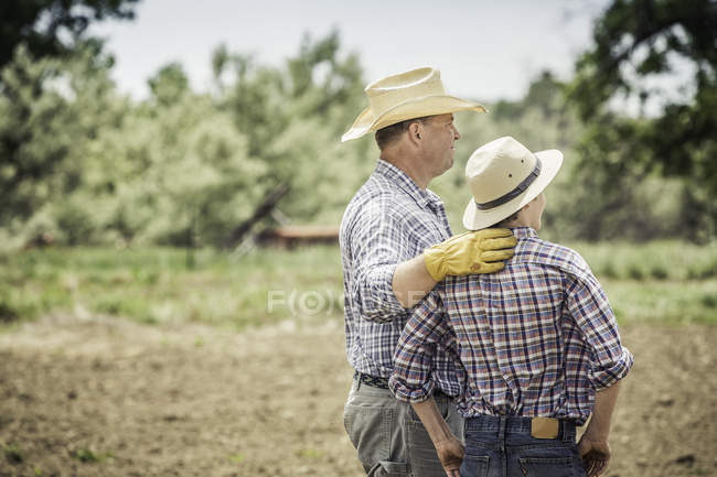 Farmer and teenage grandson looking out from ploughed field — Stock Photo