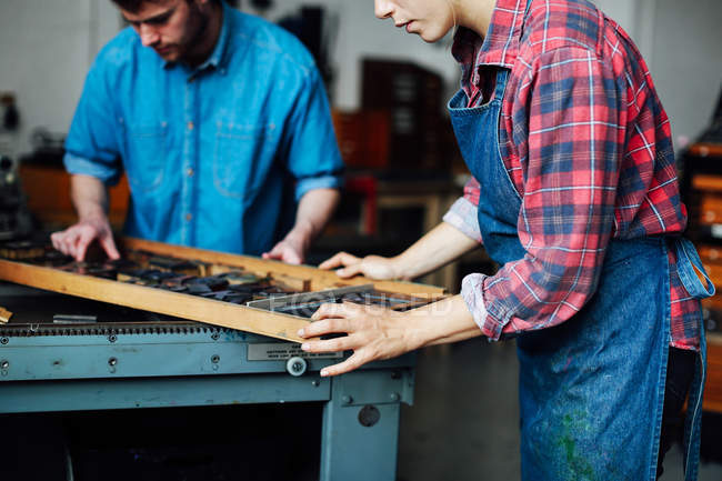 Young craftsman and craftswoman looking at letters in letterpress studio, mid section — Stock Photo