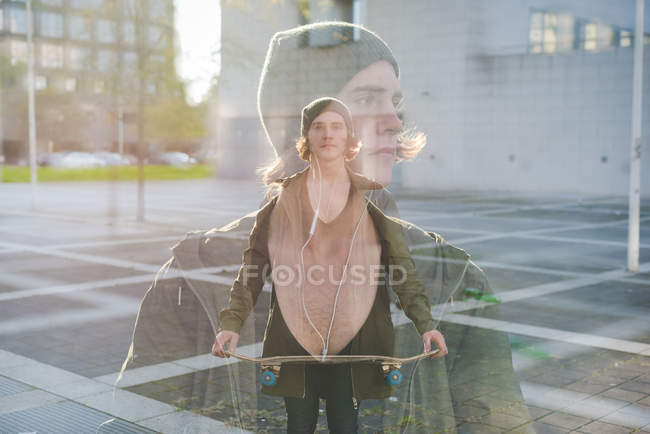 Double exposure portrait of cool young male skateboarder near tower block — Stock Photo