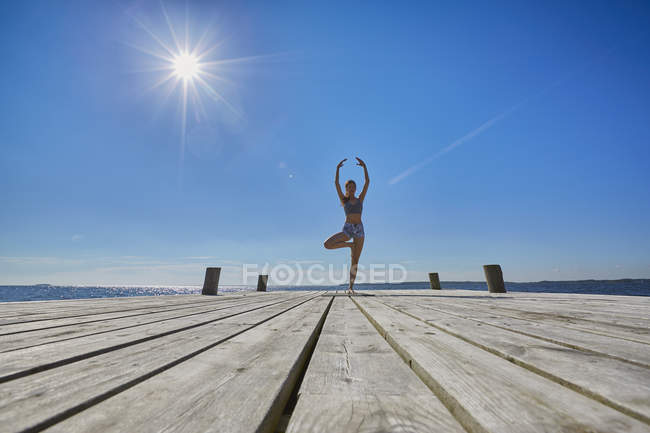 Середній вид жінки на пірсі, що стоїть на одній нозі підняті руки — стокове фото