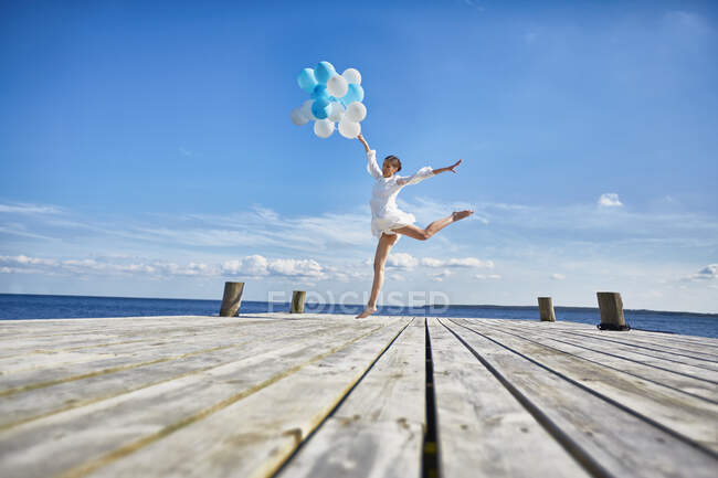 Jeune femme dansant sur une jetée en bois, tenant un tas de ballons — Photo de stock