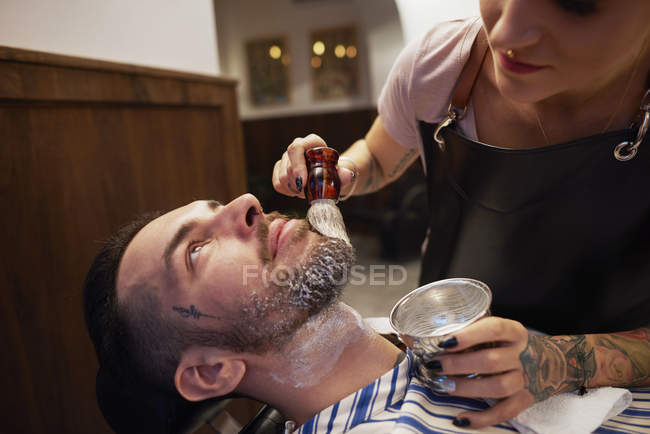 Женщина наносит крем для бритья на бороду мужчины — стоковое фото