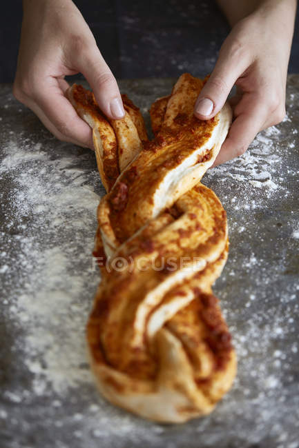 Mains féminines tressant la pâte à pain à la cannelle — Photo de stock