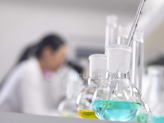 A scientist looking down a microscope with a chemical formula in the foreground — Stock Photo