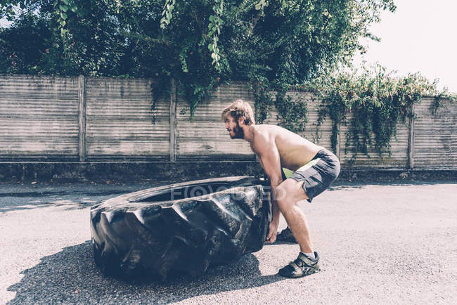 Молодой тренер по кроссу поднимает тяжелые шины у спортзала — стоковое фото
