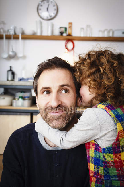 Girl whispering to father in kitchen — Stock Photo