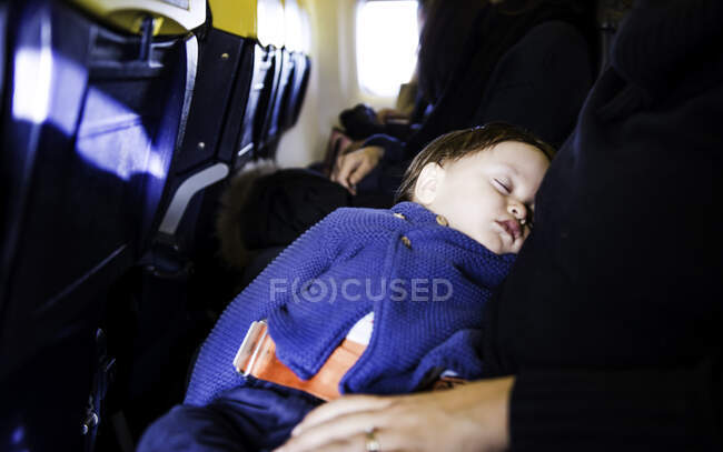 Menino dormindo no joelho da mãe em voo de avião — Fotografia de Stock
