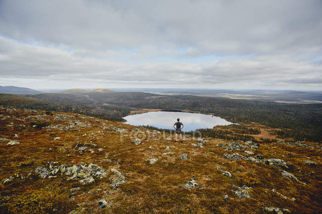 Rückansicht eines jungen Mannes, der in ländlicher Landschaft mit See steht — Stockfoto
