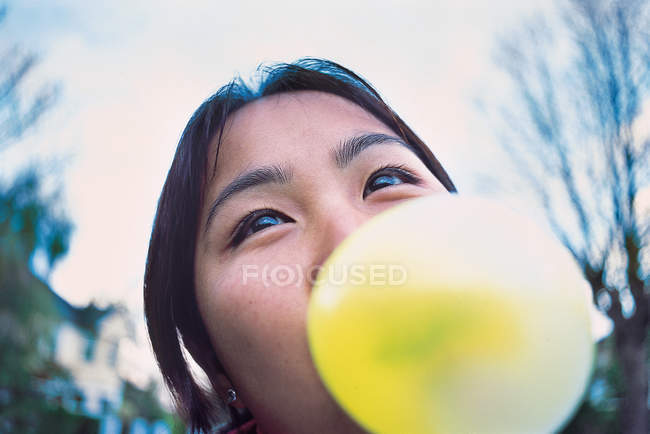 Primer plano de mujer joven soplando burbuja de goma de mascar amarilla - foto de stock