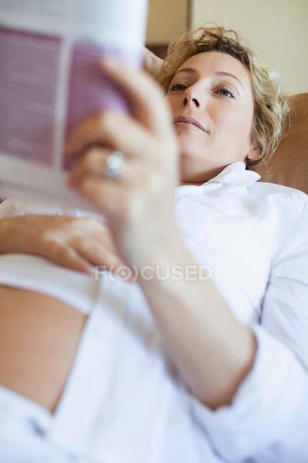 Femme enceinte lisant sur le canapé — Photo de stock