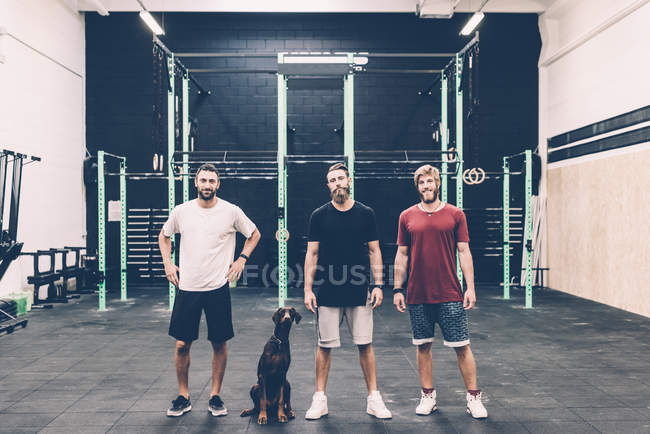 Retrato de três treinadores cruzados masculinos e cão no ginásio — Fotografia de Stock