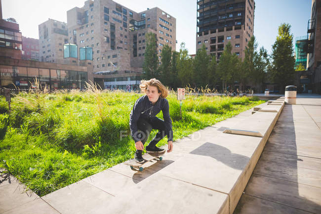 Giovane skateboarder maschile accovacciato mentre skateboard su muro urbano — Foto stock