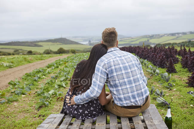 Casal em local rural sentado em paletes olhando para longe — Fotografia de Stock