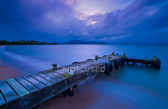 Wooden pier stretching into ocean at nighttime — Stock Photo