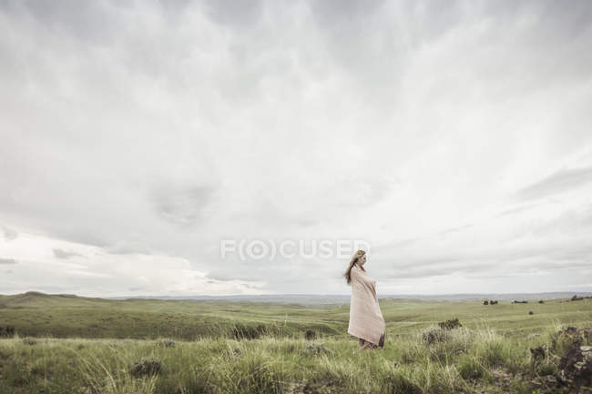 Jovem mulher envolta em cobertor rosa olhando para a paisagem, Cody, Wyoming, EUA — Fotografia de Stock