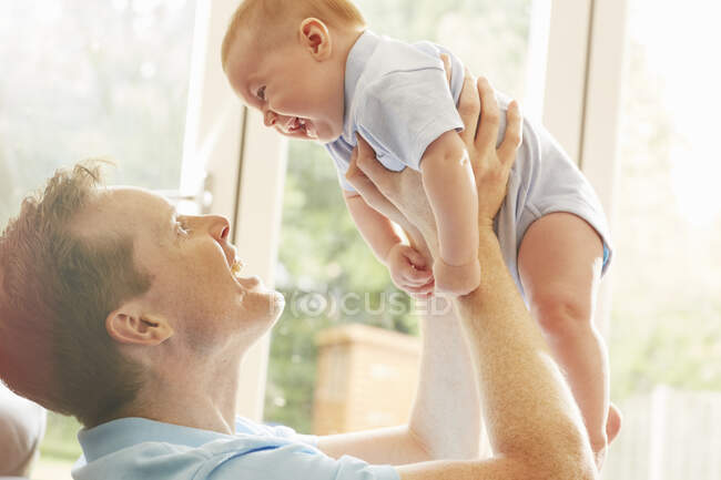 Mature man holding up baby son — Stock Photo