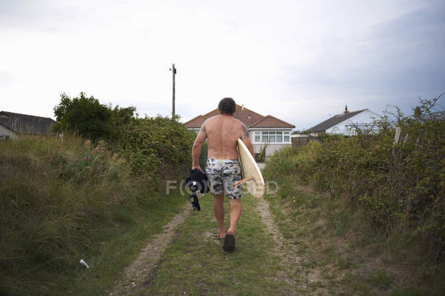 Rückansicht eines Surfers, der sein Surfbrett nach Hause trägt — Stockfoto