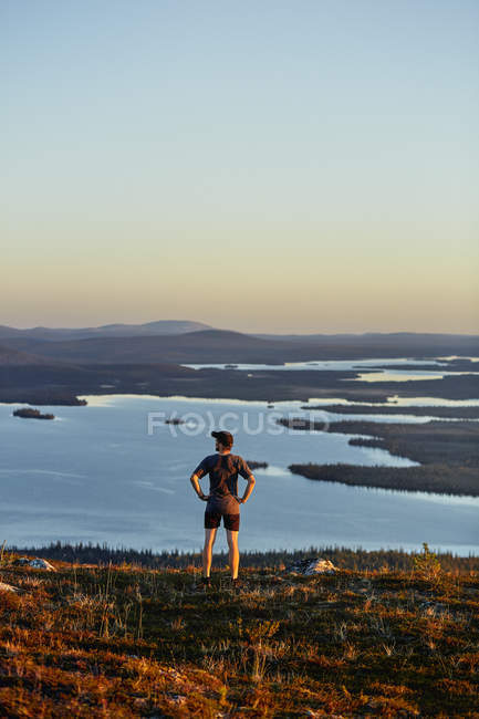 Hombre mirando hacia el lago en la cima del acantilado al atardecer, Keimiotunturi, Laponia, Finlandia - foto de stock