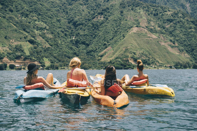 Vista trasera de cuatro amigas jóvenes haciendo kayak en el lago Atitlán, Guatemala - foto de stock