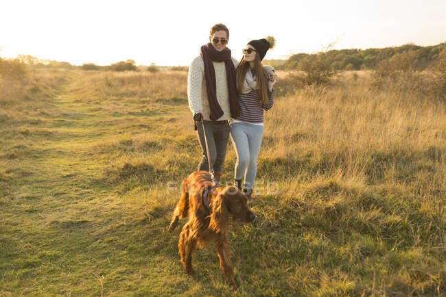 Jeune couple marchant avec chien dans le champ d'automne — Photo de stock
