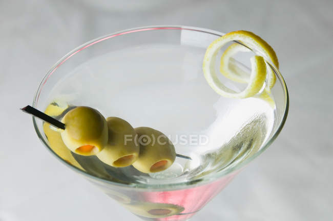 Martini drink with olives and lemon peel in glass — Stock Photo