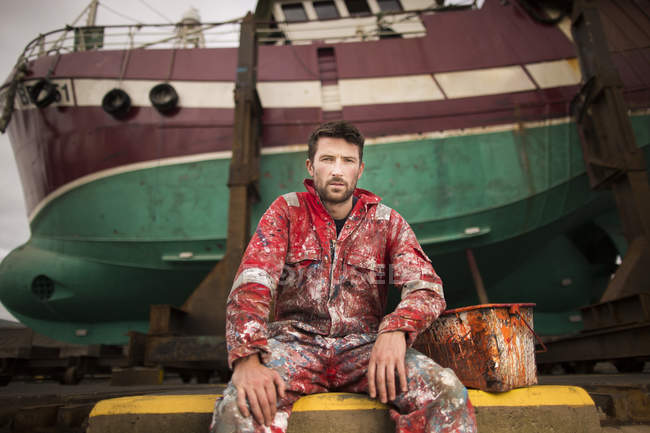 Retrato de un pintor de barcos sentado frente a un barco de pesca en el dique seco - foto de stock