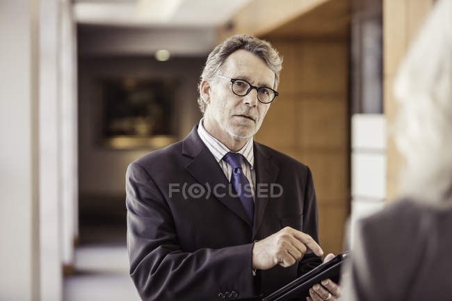 Vista por encima del hombro del hombre de negocios utilizando tableta digital en el pasillo de la oficina - foto de stock
