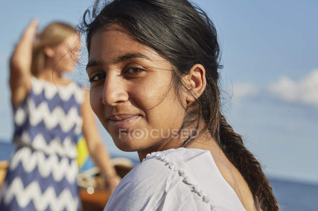 Молода жінка дивиться через плече на камеру, посміхаючись у блакитному океані — стокове фото