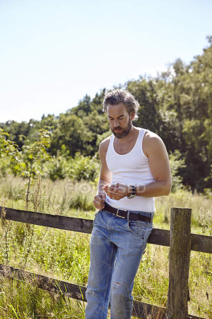 Mid adult man leaning against rural fence gazing at blade of grass — Stock Photo