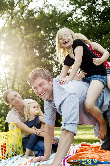 Батько, що дає донькам свинарство на сімейному пікніку в парку — стокове фото