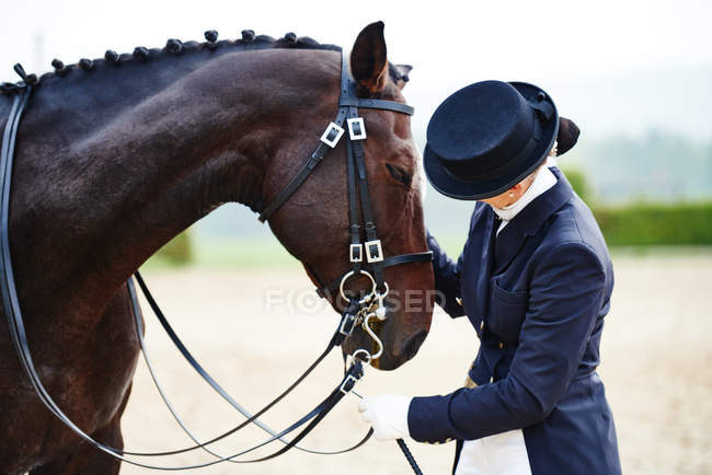 Jinete hembra acariciando caballo doma en arena ecuestre - foto de stock