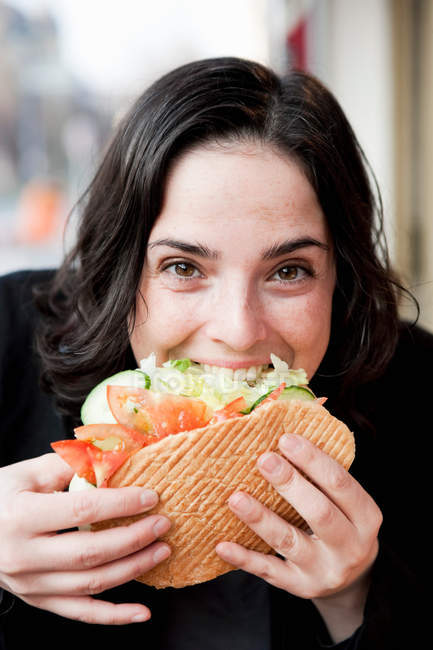 Donna che morde Sandwich e guardando la fotocamera — Foto stock
