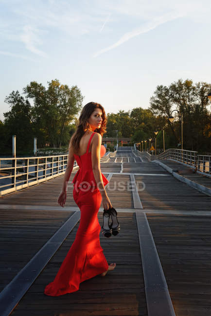Retrato de uma jovem mulher em um vestido vermelho inteligente se afastando e olhando por cima do ombro — Fotografia de Stock