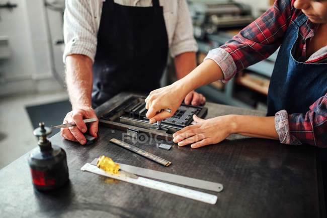 Senior craftsman working on letterpress with young craftswoman in print workshop, mid section — Stock Photo